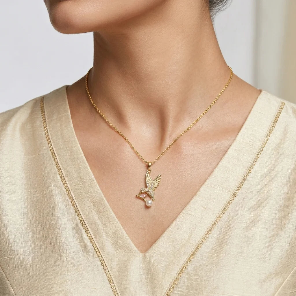 Gold necklace with a pendant worn by a person in a light-colored outfit.