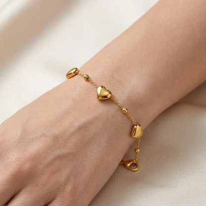 Gold bracelet with heart-shaped charms on a wrist against a neutral background