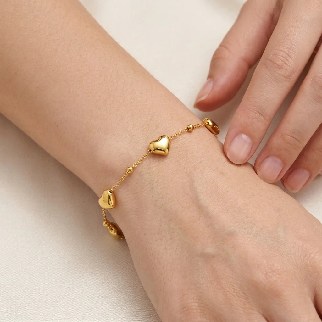 Gold bracelet with heart-shaped charms on a wrist against a neutral background