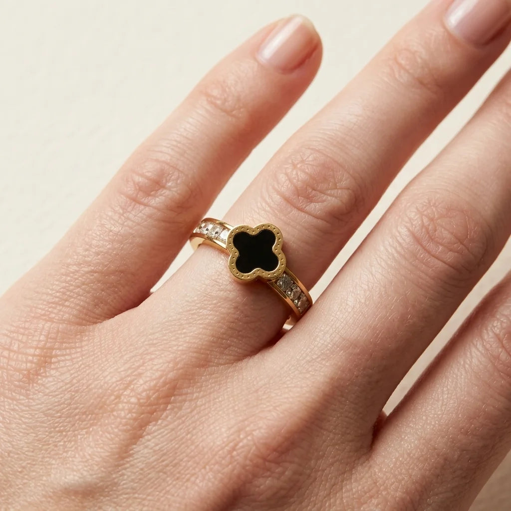 Gold ring with a black clover design on a hand against a beige background