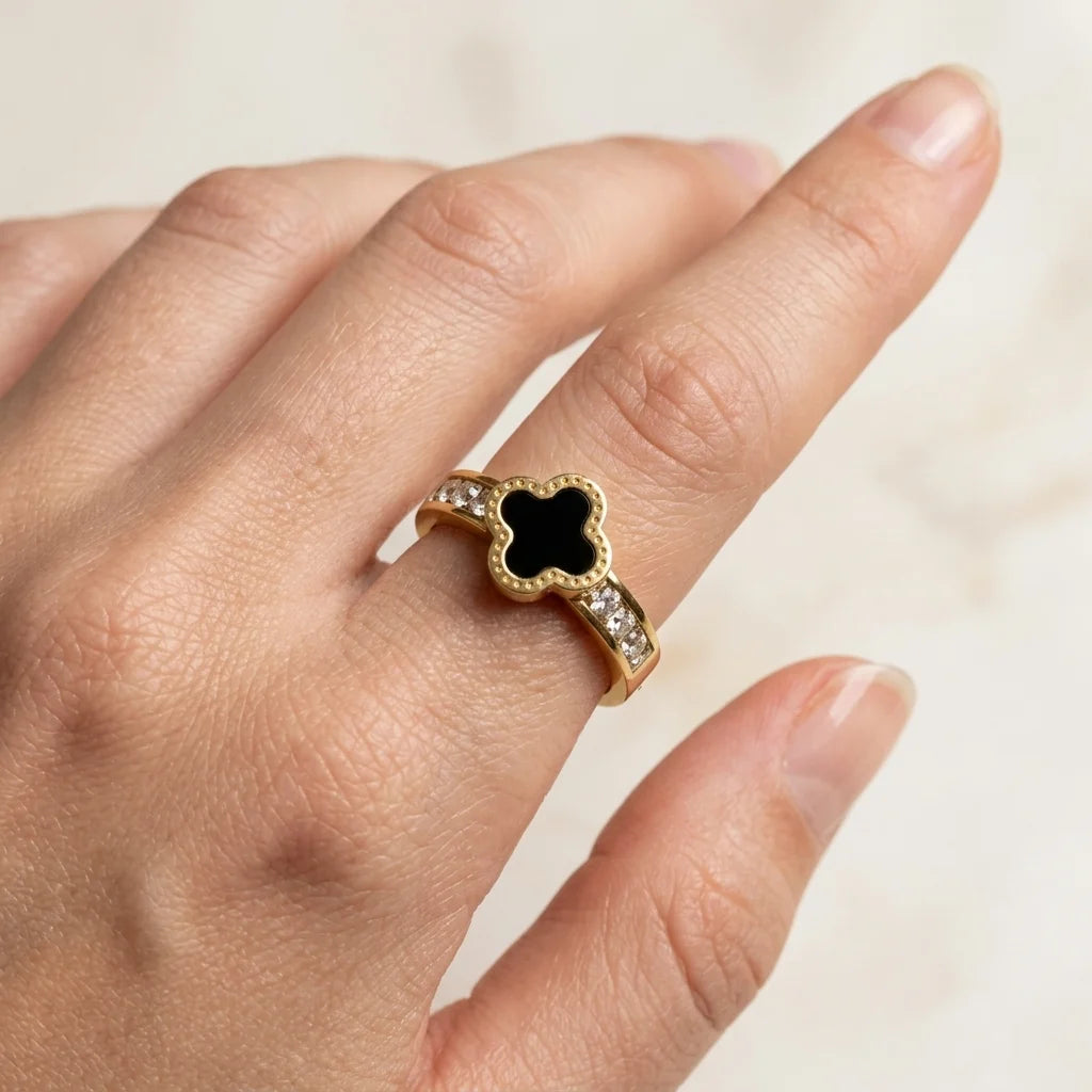 Gold ring with a black gemstone on a hand against a neutral background