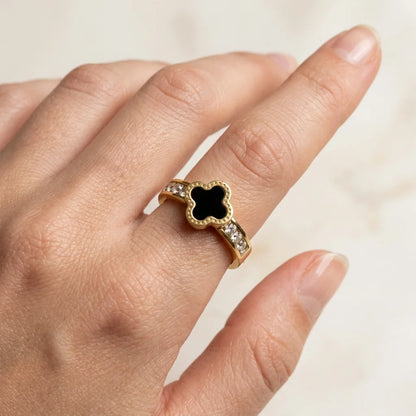 Gold ring with a black gemstone on a hand against a neutral background