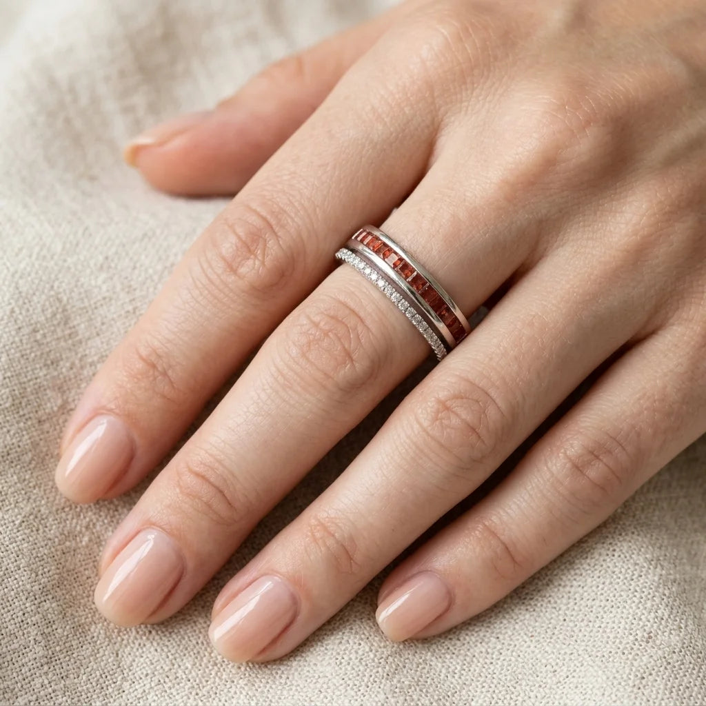 Hand wearing a silver ring with red gemstones on a beige fabric background