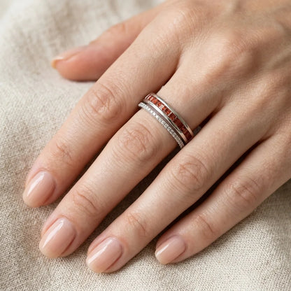 Hand wearing a silver ring with red gemstones on a beige fabric background