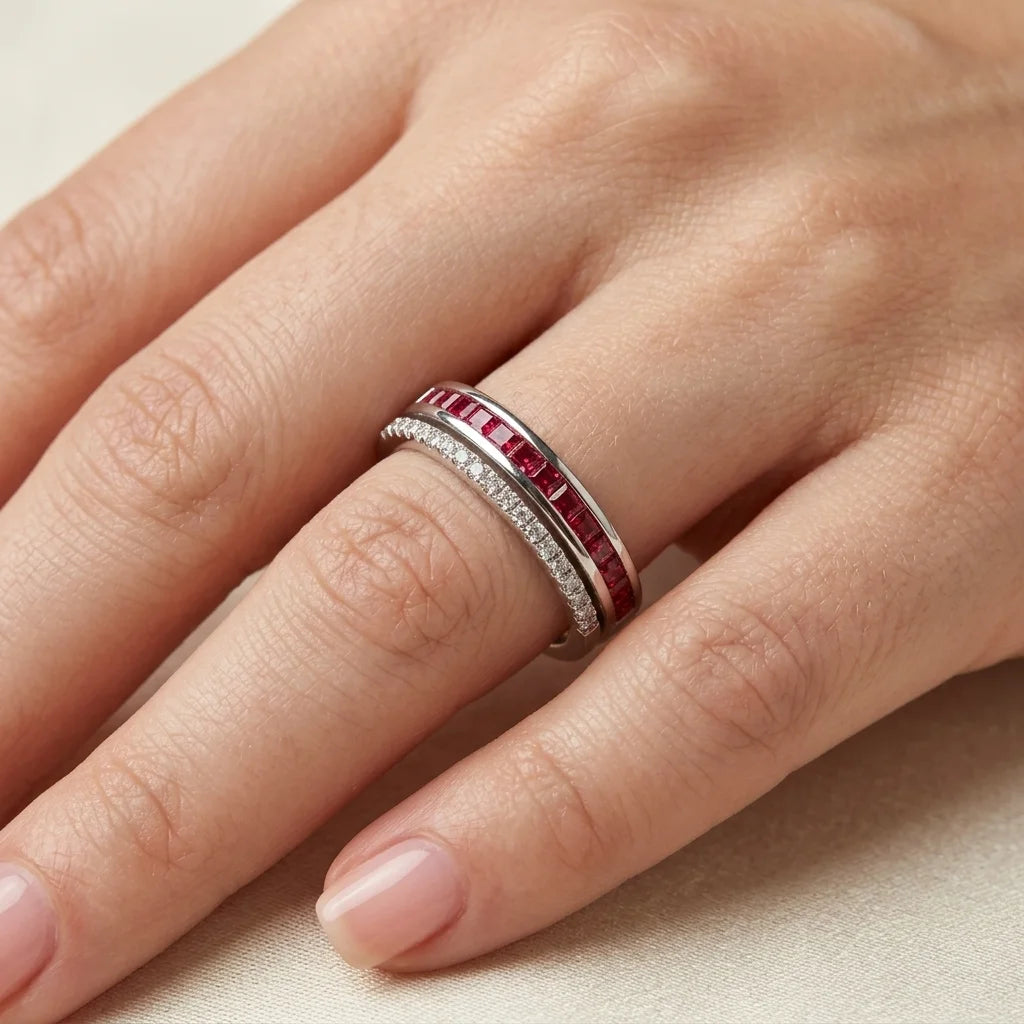 Close-up of a hand wearing a silver ring with red gemstones on a neutral background