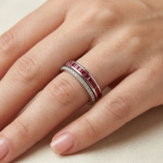 Close-up of a hand wearing a silver ring with red gemstones on a neutral background