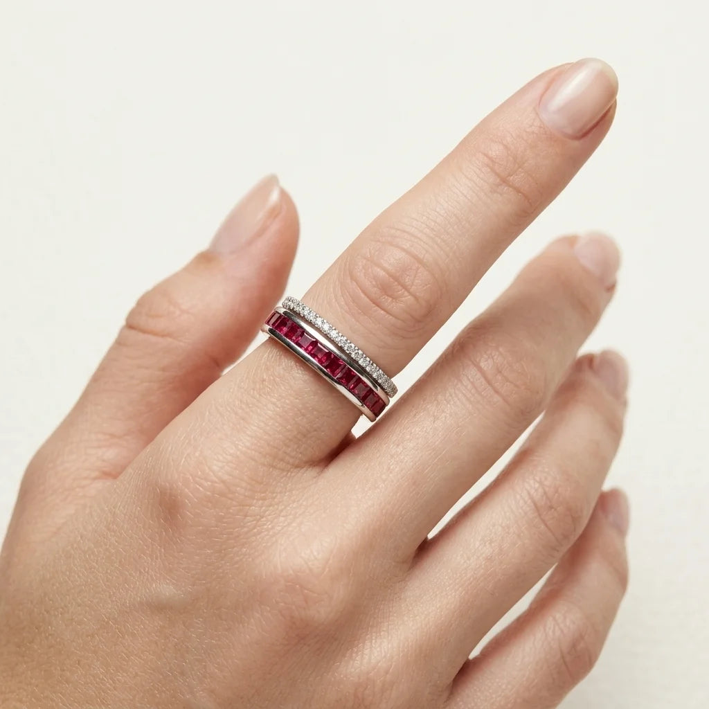 Hand wearing a ring with red gemstones on a neutral background