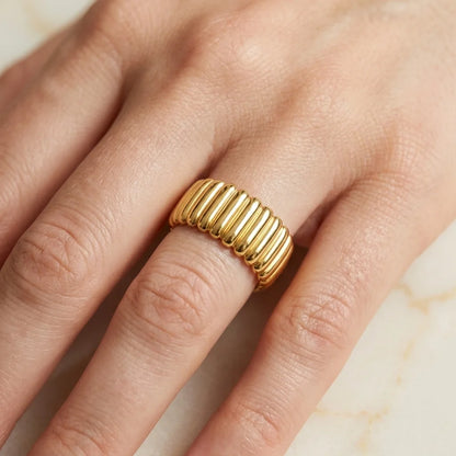 Gold ring on a finger against a neutral background
