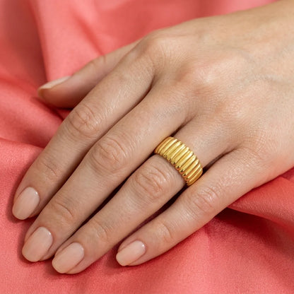 Gold ring on a hand with a pink fabric background