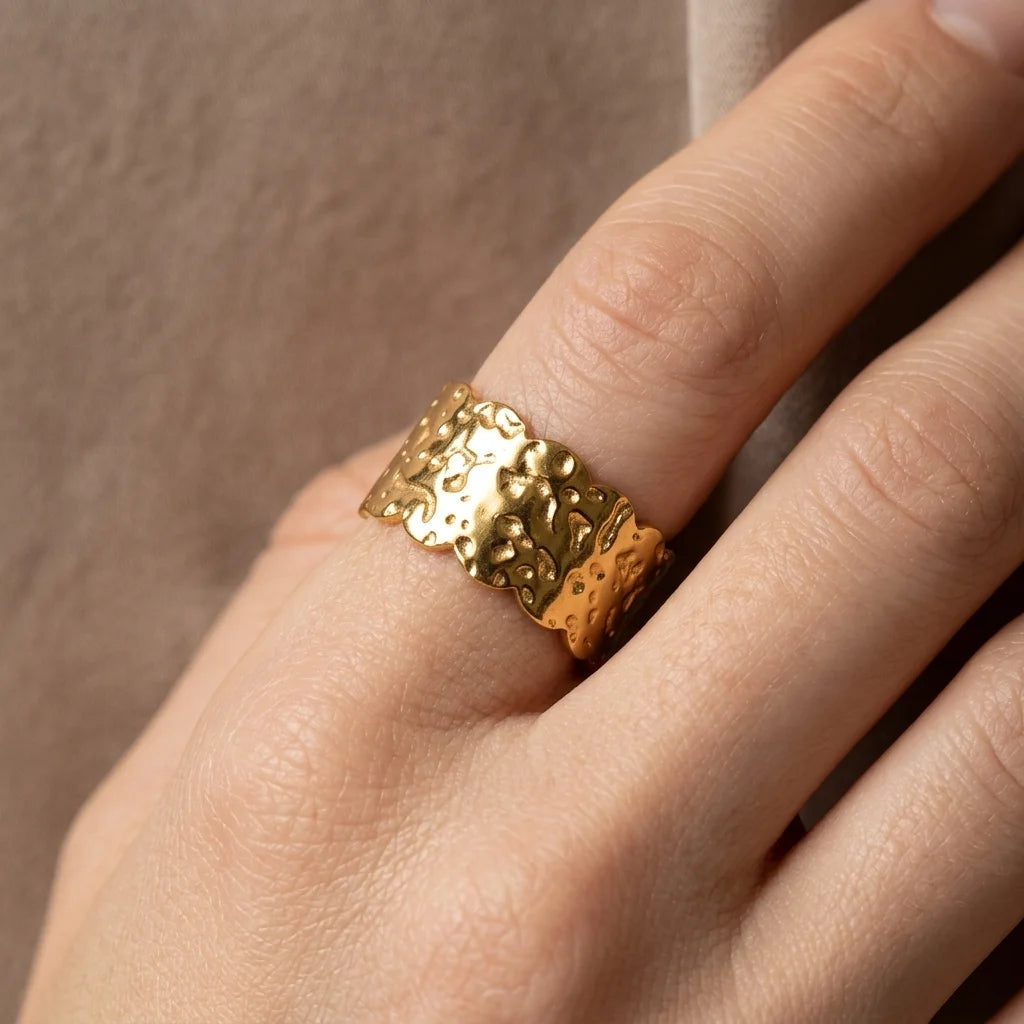 Gold textured ring on a finger against a neutral background
