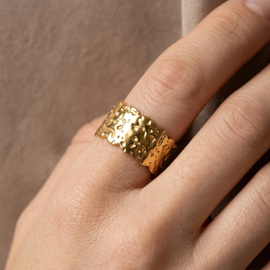 Gold textured ring on a finger against a neutral background