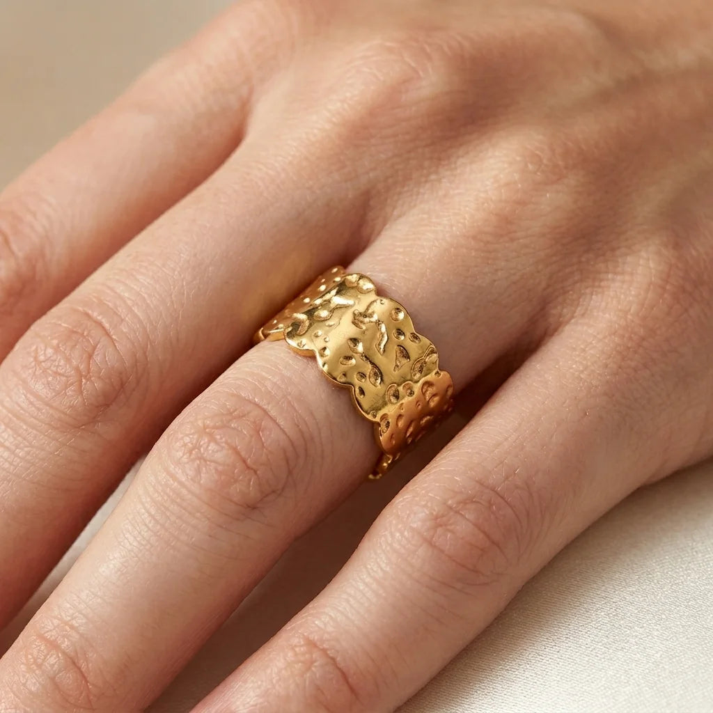 Gold ring with intricate design on a person's finger against a neutral background
