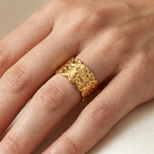 Gold ring with intricate design on a person's finger against a neutral background