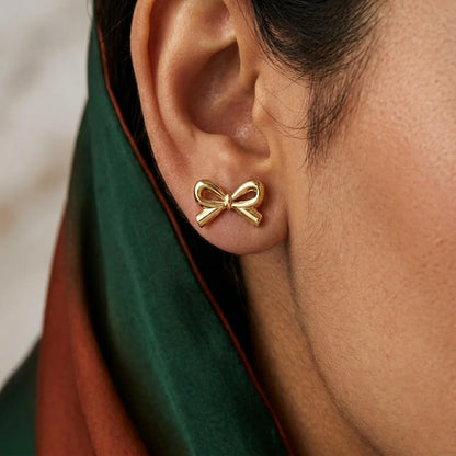 Gold bow-shaped earring worn by a person with a blurred background