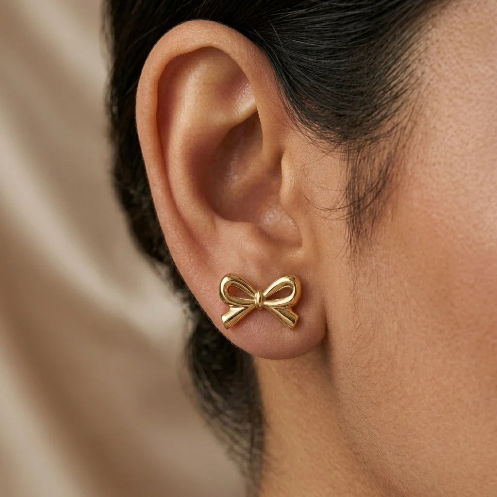 Gold bow-shaped earring worn on an ear with a neutral background
