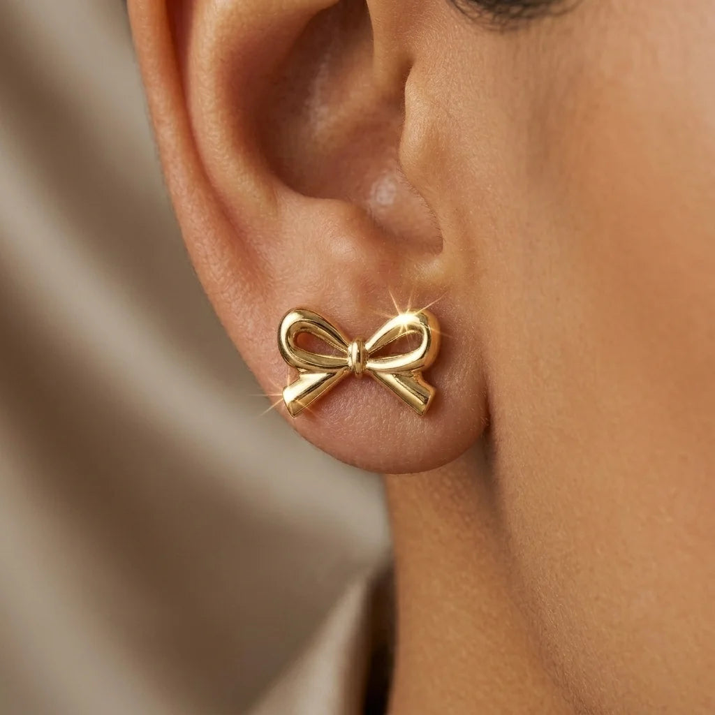 Gold bow-shaped earring worn on an ear with a neutral background