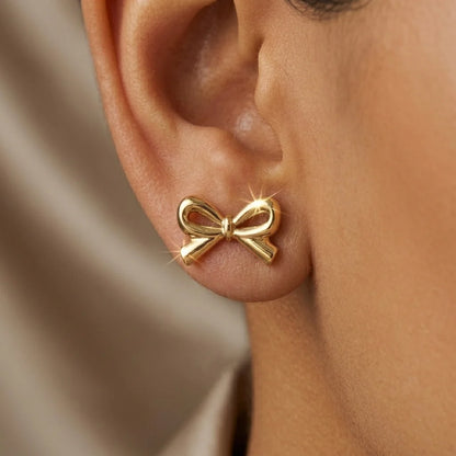 Gold bow-shaped earring worn on an ear with a neutral background