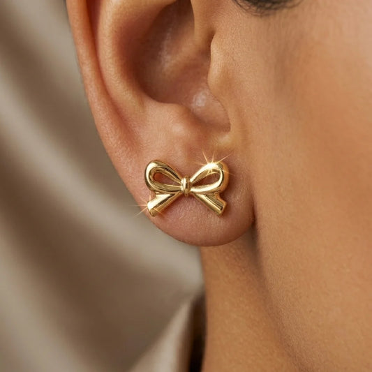 Gold bow-shaped earring worn on an ear with a neutral background