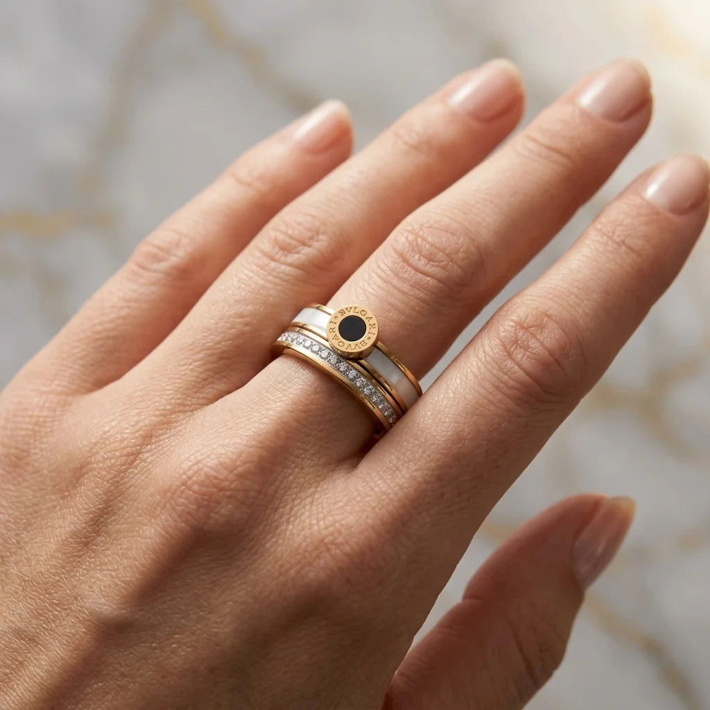 Hand wearing a gold ring with a black gemstone on a neutral background