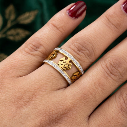 Gold ring with intricate design on a person's finger against a dark background