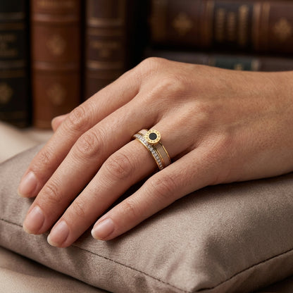 Hand wearing a gold ring with a black gemstone on a textured surface with books in the background