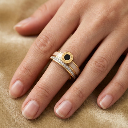 Hand wearing a gold ring with a black gemstone on a beige background