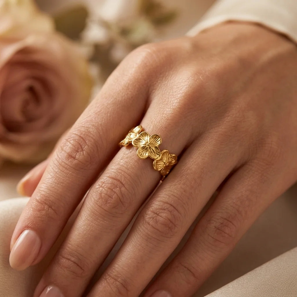 Gold floral ring on a hand with a blurred background of flowers