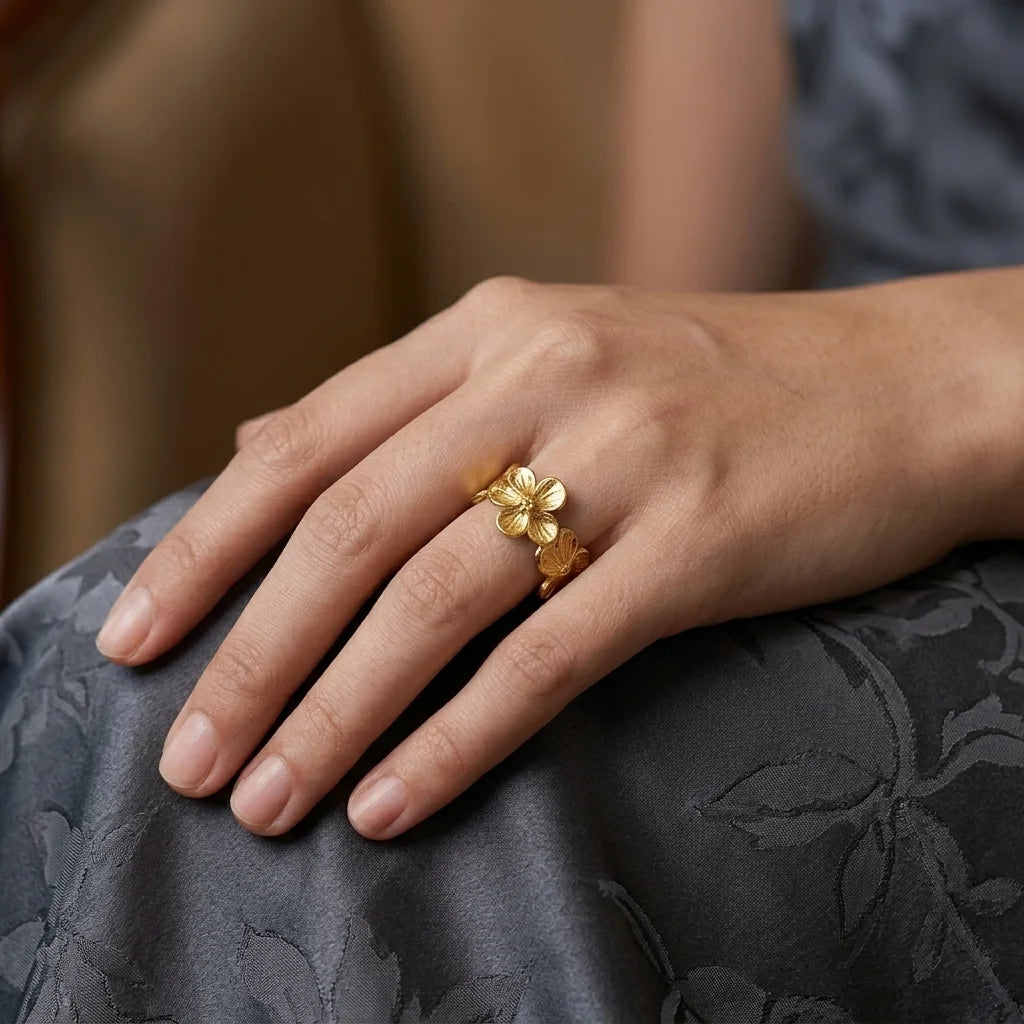 Hand wearing a gold floral ring on a dark fabric surface