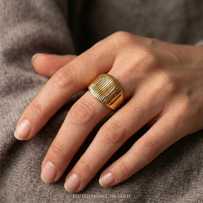 Gold ring on a person's finger against a neutral background