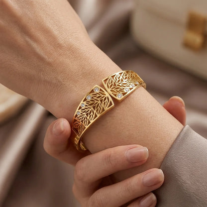 Gold bracelet with leaf design on a wrist against a neutral background