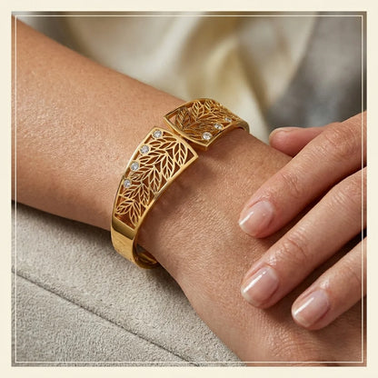 Gold bracelet with leaf design on a wrist against a neutral background