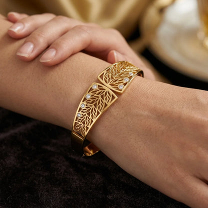 Gold bracelet with leaf design on a wrist against a dark background