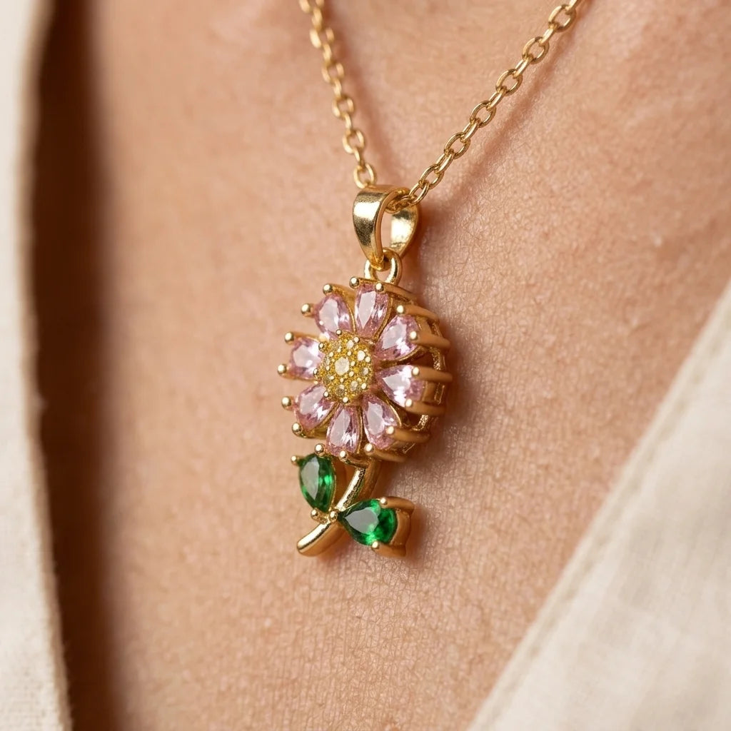 Gold necklace with a floral pendant featuring pink and green gemstones on a person's neck.