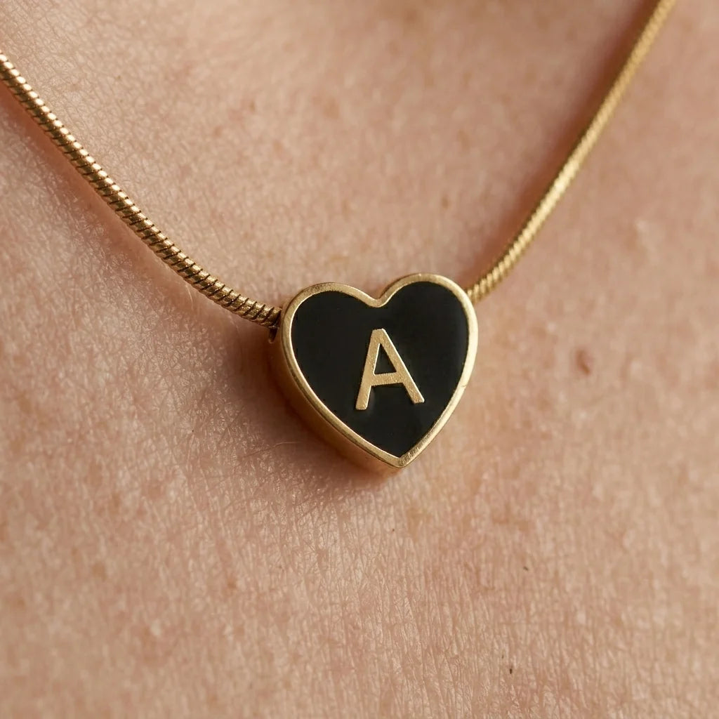 Heart-shaped necklace with a black enameled heart and gold 'A' on a skin background