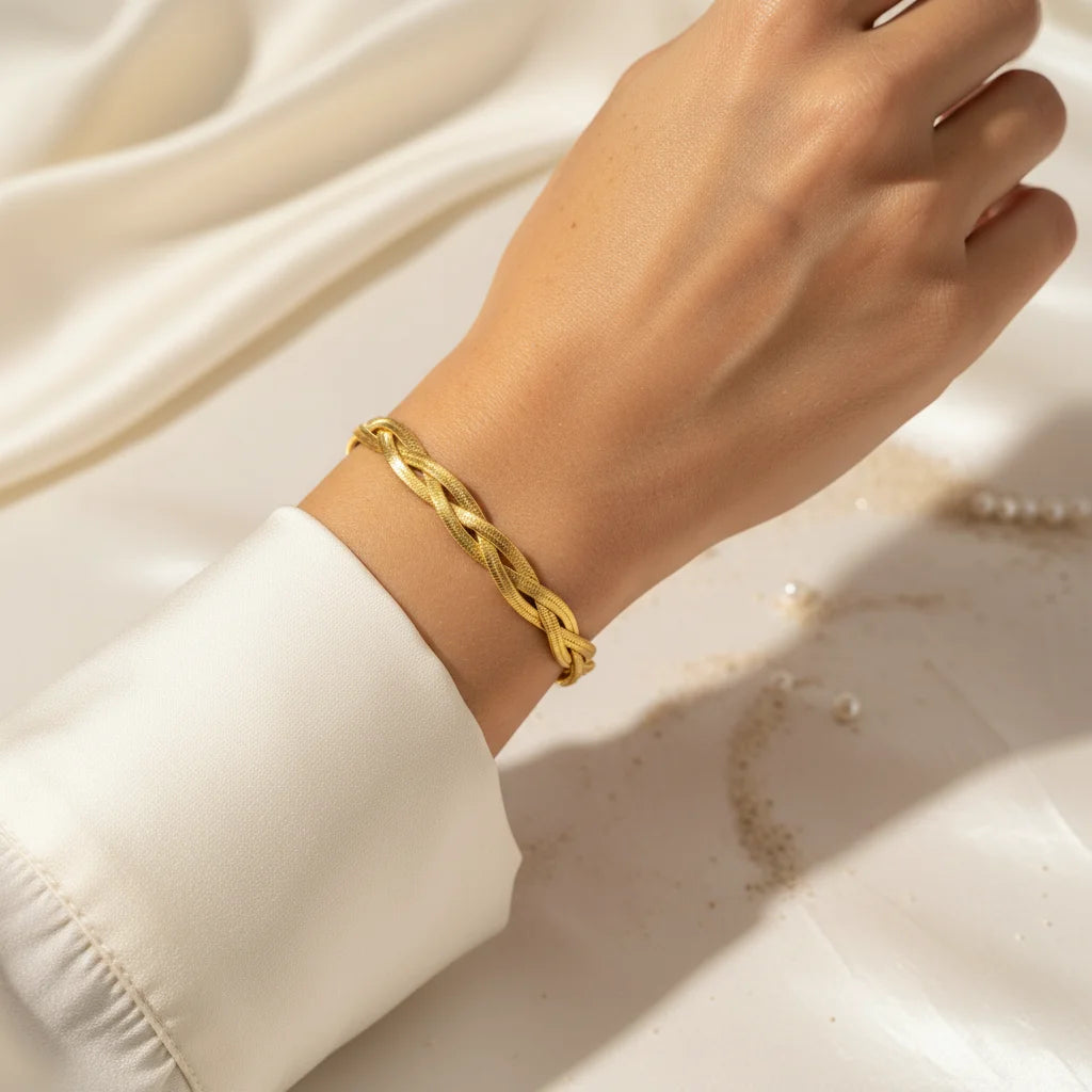 Gold braided bracelet on a person's wrist against a neutral background