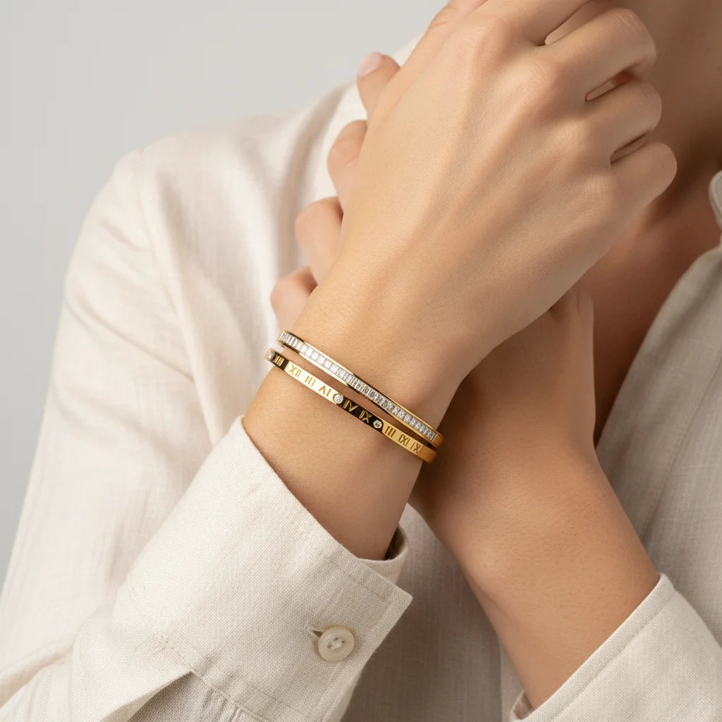 Close-up of a person's wrist wearing gold bracelets with Roman numeral designs on a neutral background.
