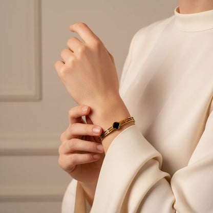 Person wearing a gold bracelet with a black stone on a neutral background