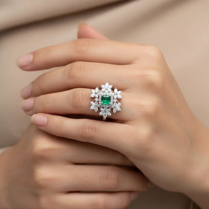 Close-up of a hand wearing an emerald and diamond ring against a beige background