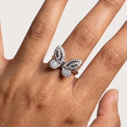 Butterfly-shaped ring with diamonds on a hand against a neutral background