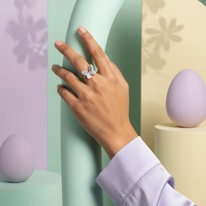 Hand wearing a decorative ring with pastel-colored eggs and geometric shapes in the background