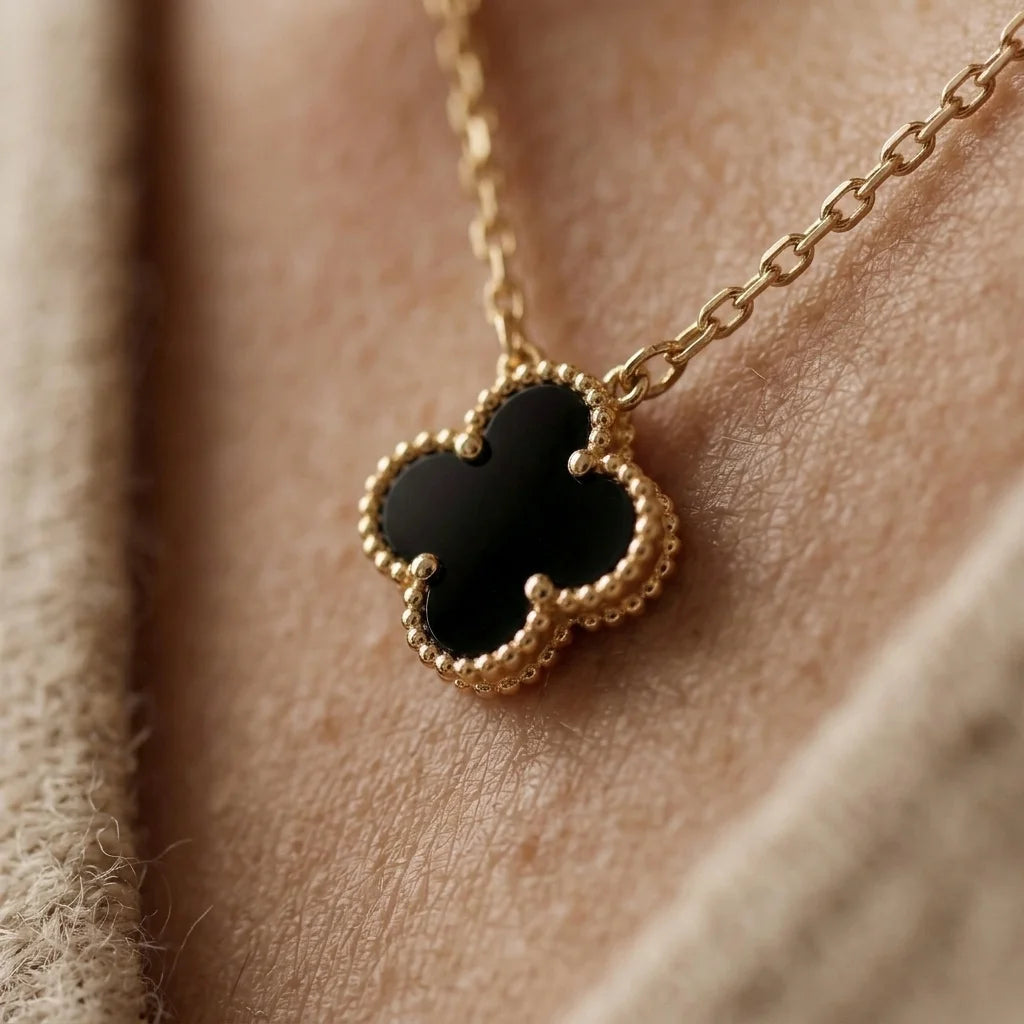 Gold necklace with a black clover pendant on a person's neck
