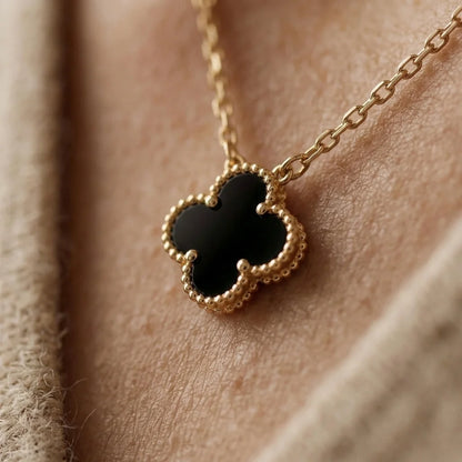Gold necklace with a black clover pendant on a person's neck