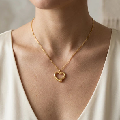 Gold heart-shaped necklace on a person wearing a white top.