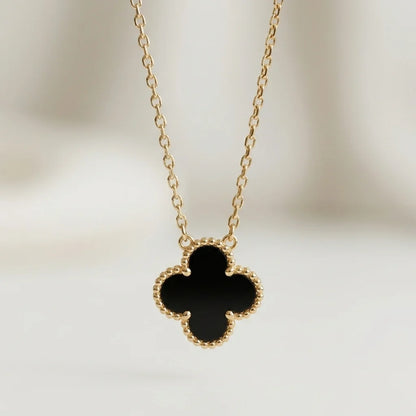 Gold necklace with a black clover pendant on a blurred background