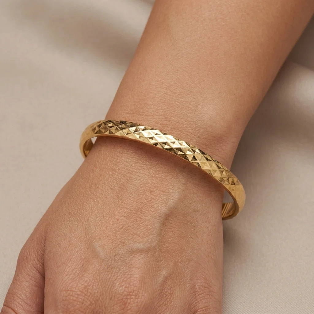 Gold bracelet on a wrist against a beige background