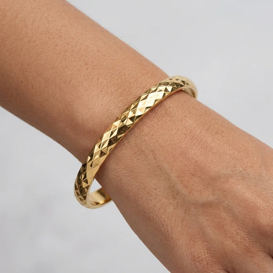 Gold bracelet on a wrist against a neutral background