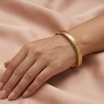 Gold bracelet on a hand against a soft pink background