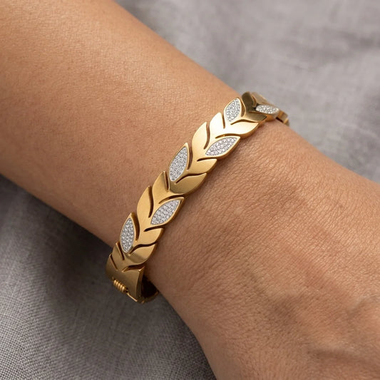 Gold bracelet with leaf design on a wrist against a gray background