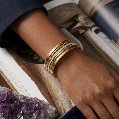 Hand wearing a gold bracelet with a book and amethyst crystal in the background