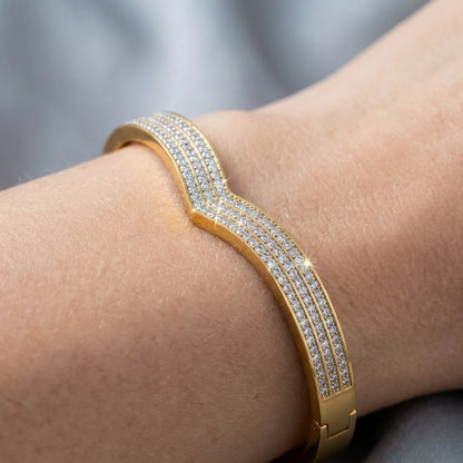 Gold bracelet with diamonds on a wrist against a neutral background